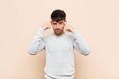 young handsome man with a serious and concentrated look, brainstorming and thinking about a challenging problem against warm wall