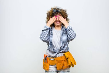 Genç hizmetçi kadın gülümsüyor ve mutlu hissediyor, iki eliyle gözlerini kapatıyor ve beyaz duvara karşı inanılmaz bir sürpriz bekliyor.