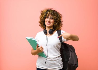 Genç, güzel, gururlu, kibirli, mutlu, şaşırmış ve tatmin olmuş görünen, kendini gösteren, pembe duvara karşı kazanan biri gibi hisseden bir öğrenci kadın.