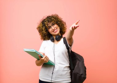 Genç, güzel bayan öğrenci neşeyle gülümsüyor sıcak, dostça, sevgi dolu bir hoş geldin sarılması yapıyor, pembe duvara karşı mutlu ve sevimli hissediyor.