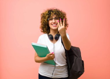 Genç, güzel bir bayan öğrenci gülümsüyor ve arkadaş canlısı görünüyor. Üç ya da üçüncüyü gösteriyor. Elleri önde, pembe duvara doğru sayıyor.