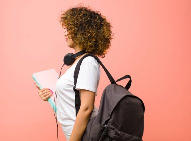 Profil görünümünde genç ve güzel bir bayan. Pembe duvarın önünde uzayı kopyalamaya çalışıyor. Düşünüyor, hayal ediyor ya da hayal ediyor.