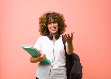 Genç ve güzel bir bayan öğrenci kendini mutlu, şaşkın, şanslı ve şaşırmış hissediyor. Sanki her şeyi ciddiye alıyormuş gibi. Pembe duvara karşı inanılmaz.