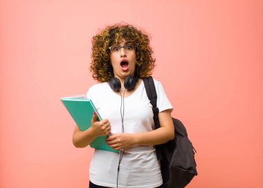 Genç ve güzel bayan öğrenci korkmuş ve şok olmuş hissediyor, ağzı açık pembe duvara karşı şaşkınlık içinde.