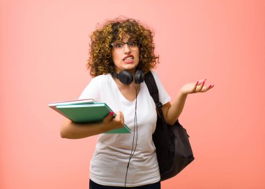 Genç ve güzel bir kız öğrenci kendini cahil ve şaşkın hissediyor. Hangi seçeneği seçeceğinden emin değil. Pembe duvara karşı merak içinde.