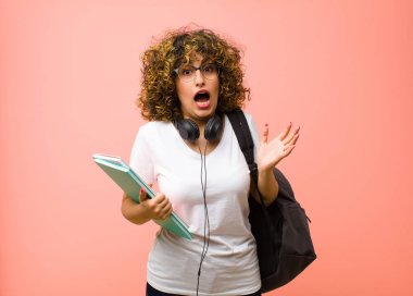 Genç ve güzel bir kadın pembe duvara karşı beklenmedik bir sürprizden dolayı şaşkın, heyecanlı, gülen, şaşkın ve mutlu hissediyor.