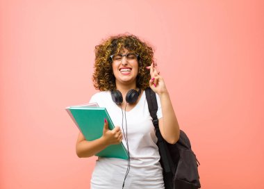 Genç ve güzel bayan öğrenci gergin ve umutlu, dua ediyor ve pembe duvara karşı iyi şanslar diliyor.