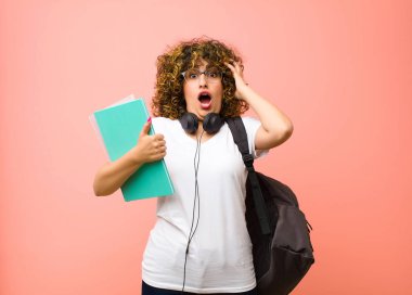 Genç ve güzel bir kız öğrenci ellerini havaya kaldırarak bağırıyor. Öfkeli, sinirli ve pembe duvara karşı üzgün hissediyor.