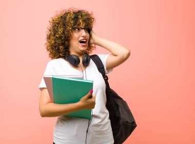 Genç ve güzel bir bayan öğrenci mutlu, heyecanlı ve şaşırmış hissediyor, yüzünü pembe duvara dayamış bir şekilde yan tarafa bakıyor.