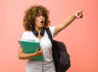 Şok olmuş ve şaşırmış hisseden genç ve güzel bir bayan. Pembe duvara karşı hayret dolu, açık ağızlı bir bakışla yukarılara bakıyor.