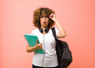 Şok olmuş, şaşırmış ve şaşırmış hisseden genç ve güzel bir bayan. Elinde pembe duvarın karşısında hayret verici, inanmayan bir bakış olan gözlükler var.