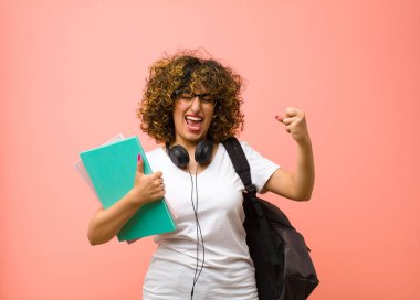 Genç ve güzel bayan öğrenci mutlu, pozitif ve başarılı hissediyor, zaferi kutluyor, başarılar ya da pembe duvara karşı iyi şanslar.