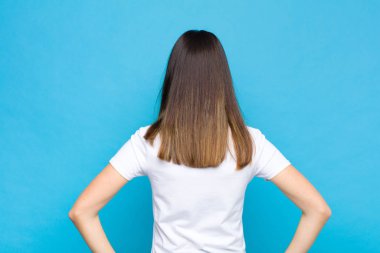 Genç, güzel bir kadın, kafası karışık ya da şüpheci ve soru dolu, merak ediyor, elleri kalçasında, dikiz aynasıyla mavi duvara bakıyor.