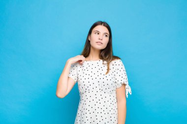 Genç, güzel bir kadın stresli, endişeli, yorgun ve hayal kırıklığına uğramış, gömleğini çekmiş, mavi duvara karşı sorunlu görünüyor.