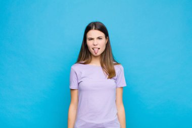 Genç, güzel bir kadın, tiksinmiş ve rahatsız olmuş hissediyor. Dilini dışarı çıkarıyor. Çirkin ve iğrenç bir şeyi mavi duvara yaslıyor.