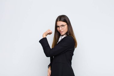 Genç iş kadını kendini mutlu, memnun ve güçlü hissediyor, kaslı ve formda, spor salonundan sonra beyaz duvara karşı güçlü görünüyor.