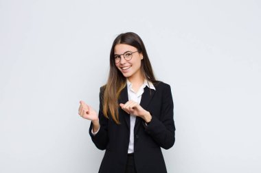 Genç iş kadını neşeli bir şekilde gülümsüyor ve yan taraftaki fotokopi alanını gösteriyor, beyaz duvara karşı mutlu ve tatmin olmuş hissediyor.