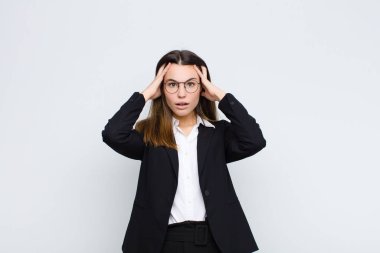 Genç iş kadını dehşete kapılmış ve şok olmuş hissediyor. Beyaz duvara karşı ellerini kaldırıyor ve panikliyor.