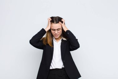 Genç iş kadını stresli ve hayal kırıklığına uğramış hissediyor, el ele tutuşuyor, yorgun, mutsuz ve migreni beyaz duvara karşı.