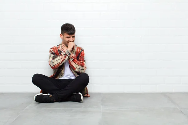 young handsome man feeling ill with a sore throat and flu symptoms, coughing with mouth covered sitting on cement floor