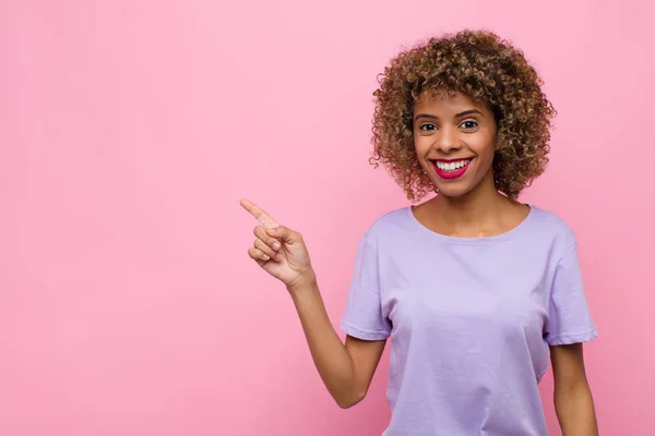 若いアフリカ系アメリカ人女性はピンクの壁にスペースをコピーするために側と上を指して興奮して驚いています — ストック写真