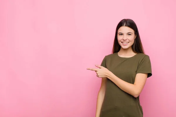 ピンクの壁にスペースをコピーするために側と上を指して興奮して驚いている若いきれいな女性 — ストック写真