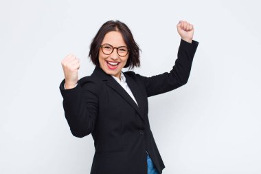 Genç iş kadını muzaffer bir şekilde bağırıyor, heyecanlı, mutlu ve şaşırmış görünüyor, beyaz duvara karşı kutlama yapıyor.