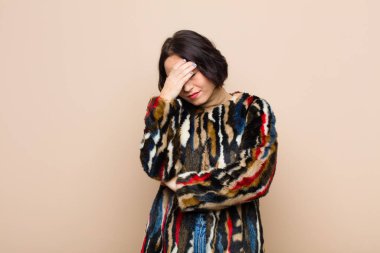 Genç, güzel bir kadın stresli, utanmış ya da üzgün görünüyor. Başı ağrıyor. Yüzü bej rengi duvarla kaplı.