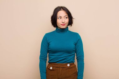 Genç, güzel bir kadın merak ediyor, mutlu düşünceler ve fikirler düşünüyor, hayal kuruyor, bej duvarlara karşı yer arıyor.