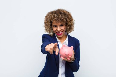 Genç Afrikalı Amerikalı bir kadın kameraya bakıyor. Tatmin olmuş, kendine güvenen, dost canlısı bir gülümsemeyle. Seni domuz kumbarasıyla seçiyor.