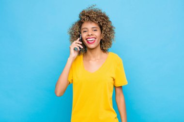 Genç Afrikalı Amerikalı mutlu ve hoş bir şekilde şaşırmış görünüyor, cep telefonuyla büyülenmiş ve şok olmuş bir ifadeyle heyecanlanıyor.