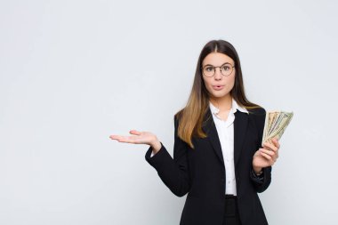 Genç ve güzel bir kadın şaşırmış ve şoka uğramış görünüyor, çenesi düşmüş, bir objeyi tutarken eli açık, banknotlar ile birlikte