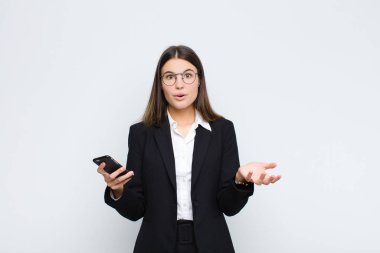 Genç ve güzel bir kadın ağzı açık ve şaşırmış, şok olmuş ve şaşırmış bir şekilde cep telefonuyla inanılmaz bir sürpriz yapmış.