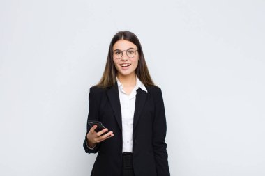 Genç ve güzel bir kadın mutlu ve hoş bir şekilde şaşırmış görünüyor, cep telefonuyla büyülenmiş ve şok olmuş bir ifadeyle heyecanlanıyor.