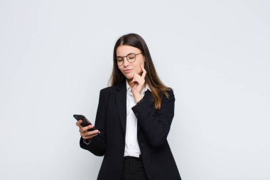 Genç, güzel bir kadın mutlu, kendinden emin bir ifadeyle gülümsüyor. Elleri çenesinde, merak ediyor ve cep telefonuyla yan tarafa bakıyor.