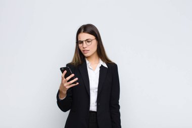 Genç, güzel bir kadın şaşkın ve şaşkın hissediyor, aptal, afallamış bir ifadeyle beklenmedik bir şeye bakıyor cep telefonuyla.