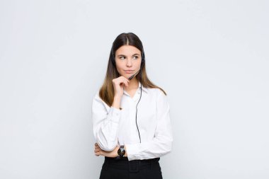 Genç, güzel bir kadın, mutlu, kendinden emin bir ifadeyle gülümsüyor. Elleri çenesinde, kulaklıklar ve mikrofonla bir tarafa bakıyor ve merak ediyor.