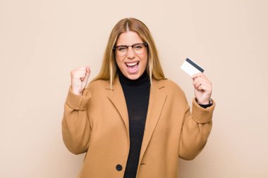 Genç sarışın kadın şok olmuş, heyecanlı ve mutlu, gülüyor ve başarıyı kutluyor, vay canına! Kredi kartıyla.