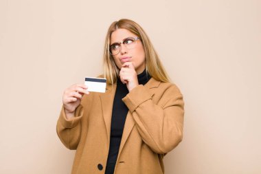 Genç sarışın kadın düşünüyor, kuşkulu ve şaşkın hissediyor, farklı seçeneklerle, kredi kartıyla hangi kararı vereceğini merak ediyor.