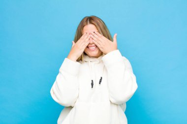 Genç sarışın kadın gülümsüyor ve mutlu hissediyor, iki eliyle gözlerini kapatıyor ve düz duvara karşı inanılmaz bir sürpriz bekliyor.