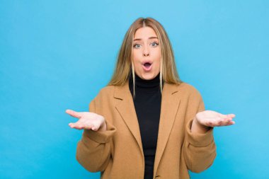 Genç sarışın kadın ağzı açık ve şaşırmış, şaşırmış ve şaşırmış bir şekilde düz duvara karşı inanılmaz bir sürprizle