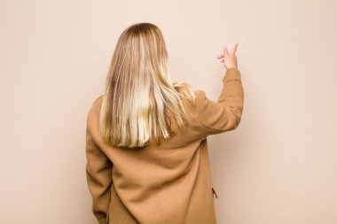 Genç sarışın kadın ayakta duruyor ve fotokopi alanındaki objeyi işaret ediyor, düz duvara karşı dikiz manzarası