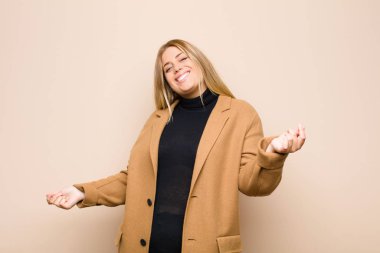 Genç sarışın kadın gülümsüyor, kaygısız hissediyor, rahat ve mutlu, dans ediyor ve müzik dinliyor, düz duvara karşı bir partide eğleniyor.