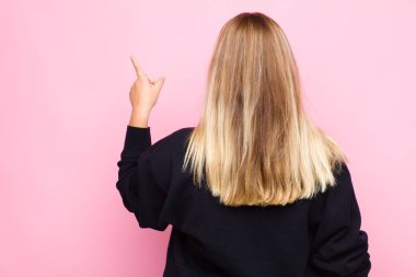 Genç sarışın kadın ayakta duruyor ve fotokopi alanındaki objeyi işaret ediyor, düz duvara karşı dikiz manzarası