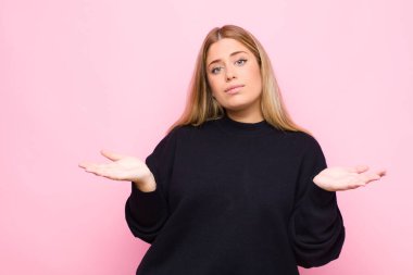 Genç sarışın kadın şaşkın ve şaşkın hissediyor, doğru cevap ya da karardan emin değil, düz duvara karşı bir seçim yapmaya çalışıyor.