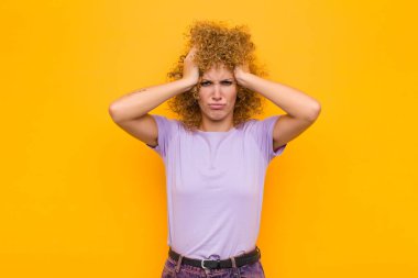 Genç afro kadın hayal kırıklığına uğramış ve sinirlenmiş, başarısızlıktan bıkmış, turuncu duvara karşı sıkıcı, sıkıcı görevlerden bıkmış