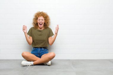 Genç afro kadın son derece mutlu ve şaşırmış görünüyor, başarıyı kutluyor, bağırıyor ve zıplıyor.