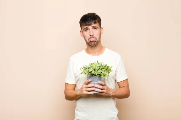 不幸そうな顔をした若いハンサムな男が植物を抱いて否定的で不満そうな態度で泣いている — ストック写真