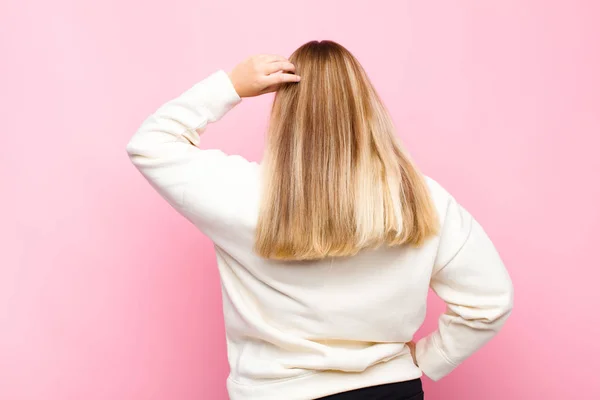 若いブロンドの女性は混乱し混乱し 解決策を考え 腰などを頭の上に手で 平らな壁に対するリアビュー — ストック写真