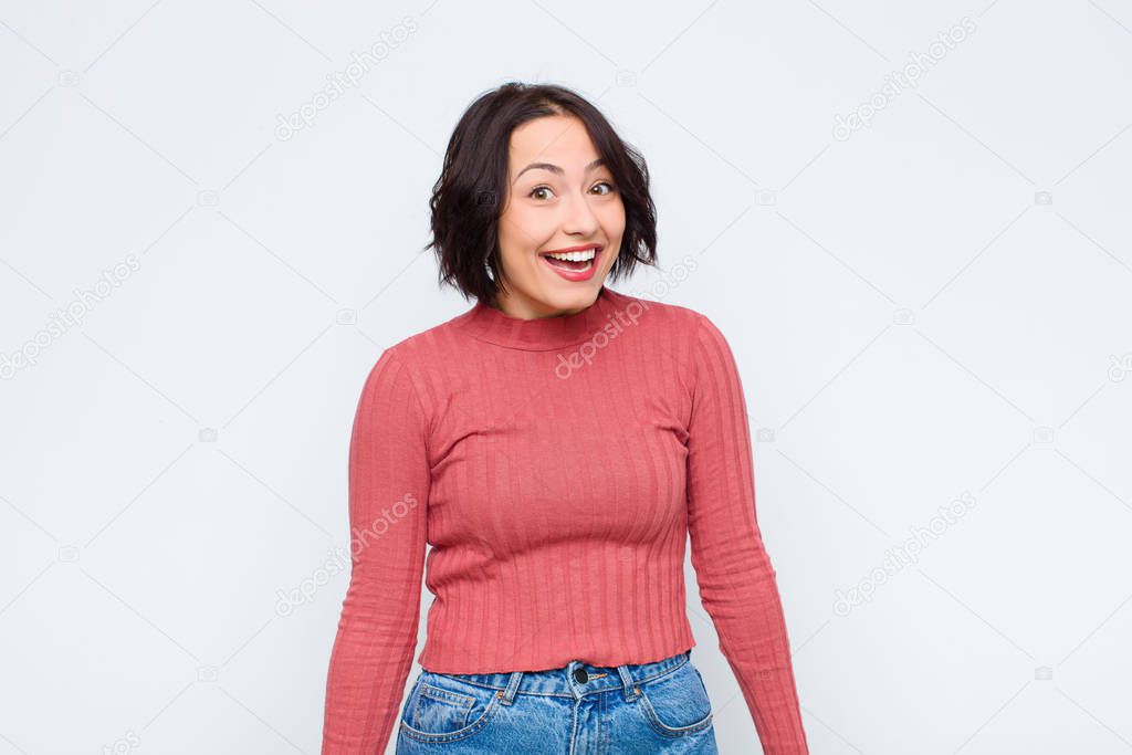 young pretty woman with a big, friendly, carefree smile, looking positive, relaxed and happy, chilling against white wall